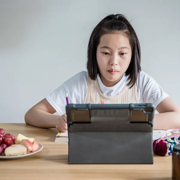 Bé gái học bài trên máy tính bảng ở bàn ăn