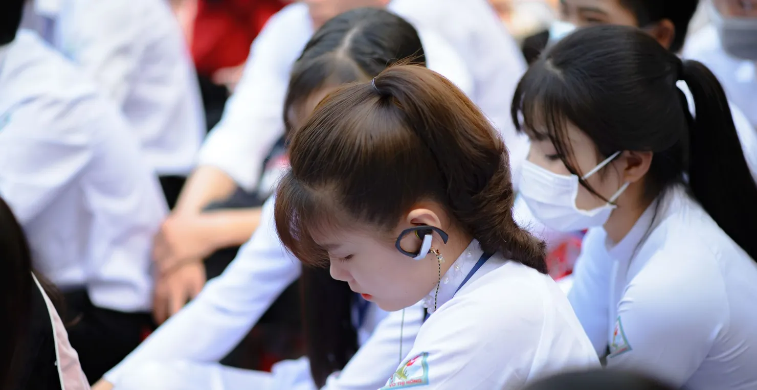 Nữ sinh áo dài trắng đeo tai nghe, cầm điện thoại giữa buổi sinh hoạt ngoài trời