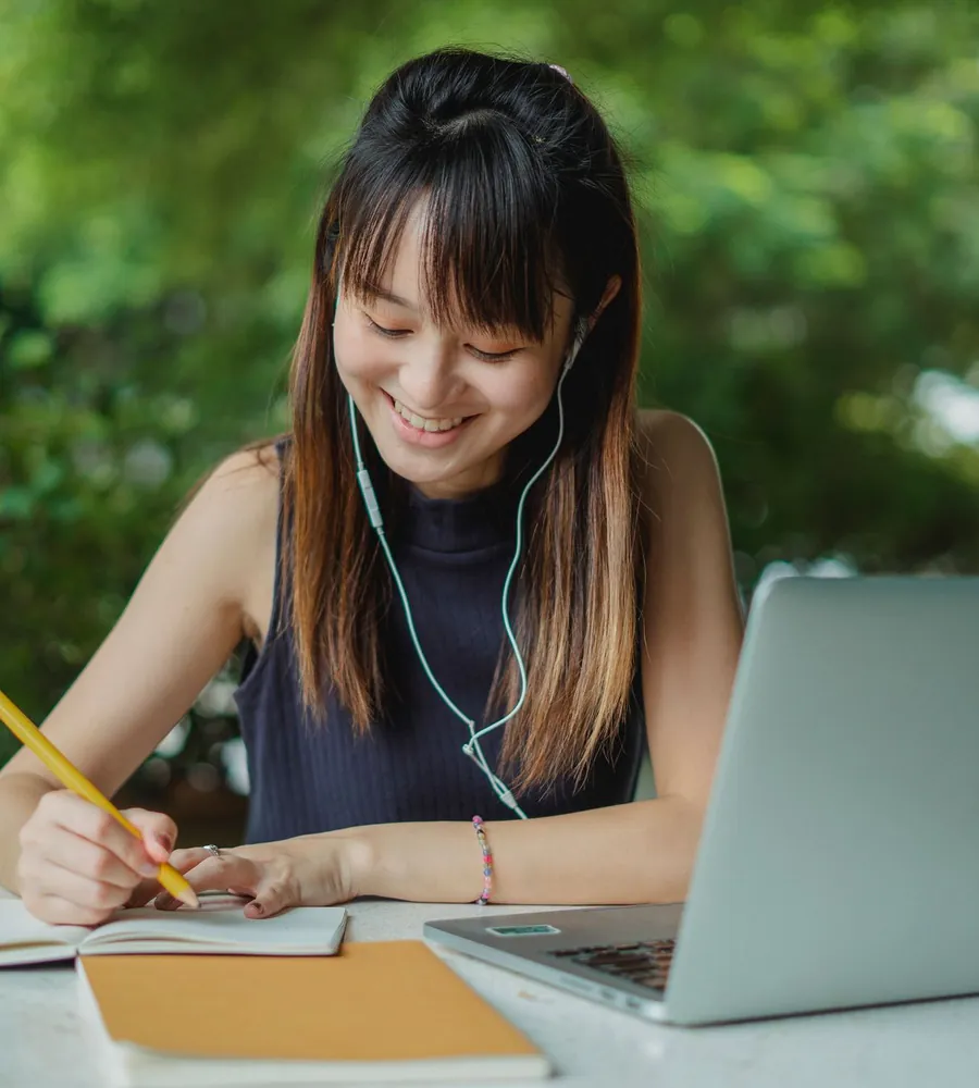 Học sinh đeo tai nghe vừa ghi chép vừa xem bài trên máy tính xách tay